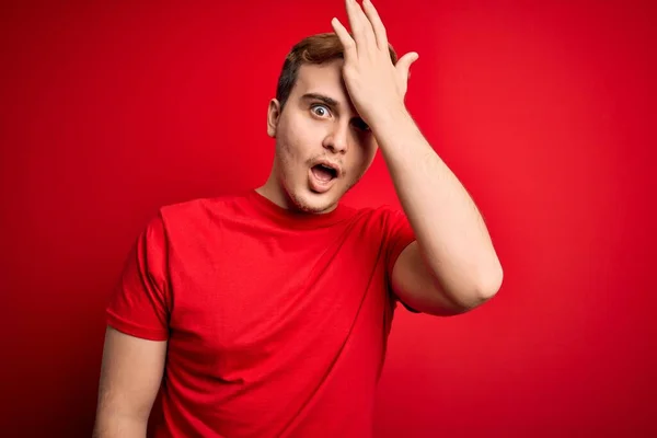 Young handsome redhead man wearing casual t-shirt over isolated red background surprised with hand on head for mistake, remember error. Forgot, bad memory concept.