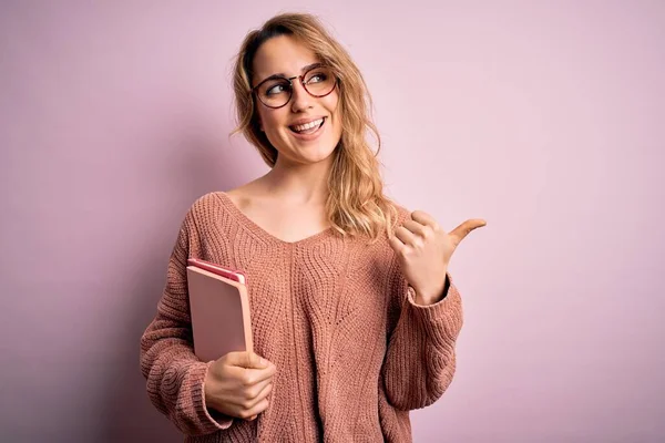 Fiatal Gyönyörű Szőke Visel Szemüveg Gazdaság Notebook Felett Rózsaszín Háttér — Stock Fotó