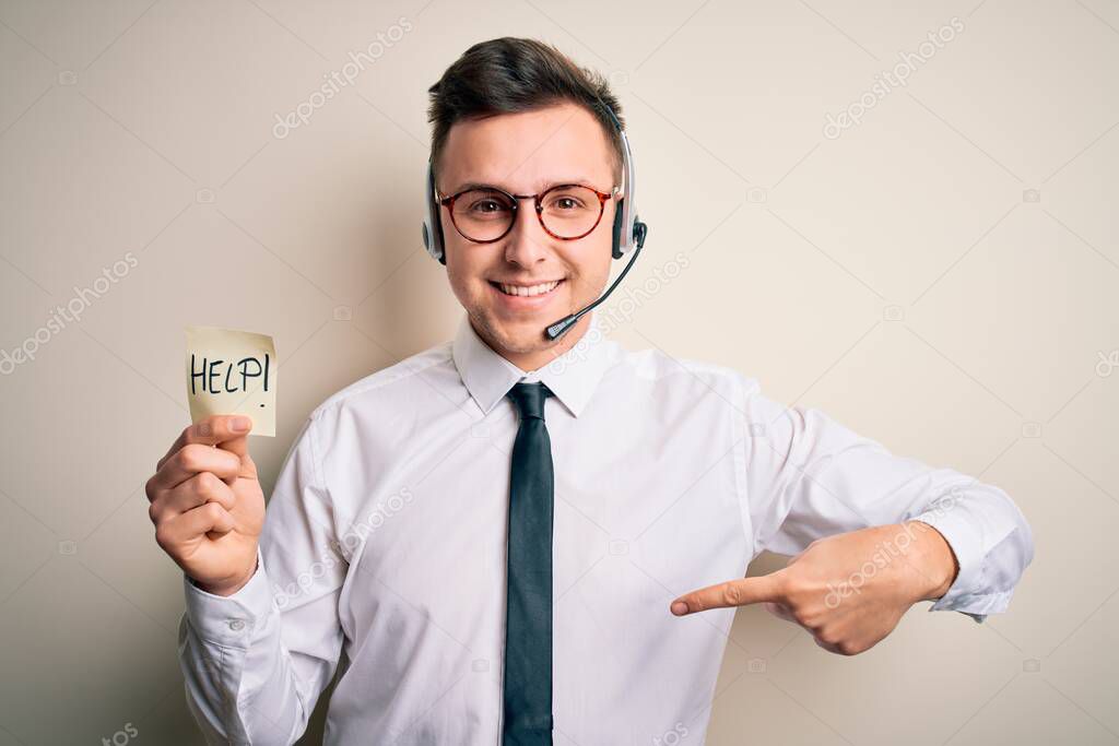 Young call center operator man wearing headset holding paper note with help word with surprise face pointing finger to himself