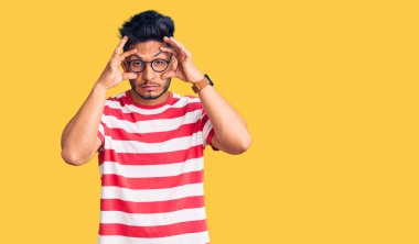 Yakışıklı Latin Amerikalı genç adam günlük kıyafetler ve gözlük takıyor parmaklarıyla gözlerini açmaya çalışıyor, uykulu ve yorgun sabah yorgunluğu için 