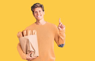 Elinde ekmek torbası olan genç yakışıklı bir adam bir fikre ya da soru işaretine şaşırmış ve mutlu bir yüzle işaret ediyor. 