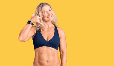 Orta yaşlı, sarışın, bikini giyen, gülümseyen, el ve parmaklarıyla telefonla konuşan bir kadın. iletişim kavramları. 