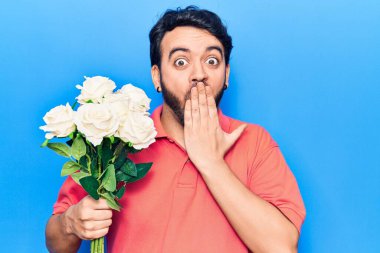 Ağzı eliyle kaplayan çiçekleri tutan genç İspanyol adam, şaşırdı ve hata yapmaktan korktu. şaşırmış ifade 