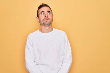 Mavi gözlü, sıradan bir süveter giyen, sarı arka planda duran, gülümseyen ve kafasını çeviren genç yakışıklı bir adam..