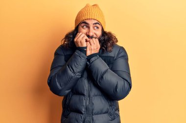 Gündelik kışlık giysiler giyen genç bir Arap. Ağzı tırnak yiyen elleri yüzünden gergin ve stresli görünüyor. anksiyete. 