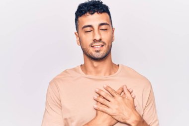 Gündelik kıyafetler giyen genç İspanyol adam elleri göğsünde gülümsüyor, gözleri kapalı ve yüzünde minnet ifadesi var. sağlık kavramı. 