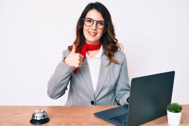 Genç, güzel esmer kadın otel resepsiyonunda mutlu ve olumlu bir şekilde gülümseyen dizüstü bilgisayar kullanıyor. 