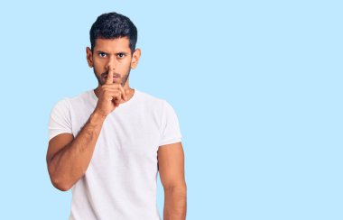 Gündelik kıyafetler giyen genç latin adam parmakları dudaklarında sessiz olmak istiyor. sessizlik ve gizli konsept. 