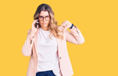 Kafkasyalı genç bir kadın akıllı telefonda konuşuyor. Kızgın bir yüz ifadesi var. Negatif işaretler baş parmakları aşağıda, reddedilme konsepti ise reddedilmiş. 