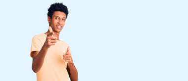 Sıradan kıyafetler giymiş genç Afro-Amerikalı adam mutlu ve komik yüzüyle kamerayı işaret ediyor. iyi enerji ve titreşimler. 