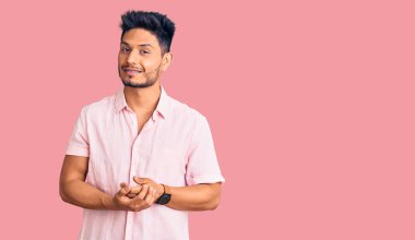 Yakışıklı Latin Amerikalı genç adam, rahat ve neşeli elleri çapraz parmaklı, sıradan bir yaz gömleği giyiyor. Başarı ve iyimserlik 