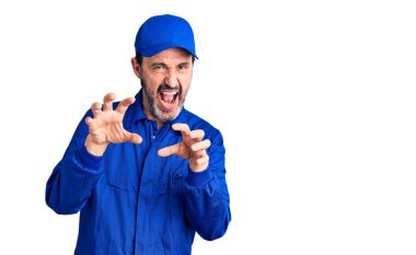 Orta yaşlı, yakışıklı, mekanik üniformalı komik gülümseyen bir adam. Pençe hareketini kedi gibi yapıyor, agresif ve seksi bir ifade. 