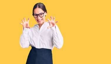 Güzel, esmer, profesyonel garson önlüğü giymiş komik bir şekilde gülümseyen, kedi gibi pençeli, agresif ve seksi bir ifade sergileyen bir kadın. 