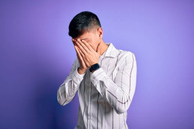 Zarif bir iş gömleği giyen genç, yakışıklı, mor arka plan üzerinde duran, ağlarken yüzünü ellerle kapatan üzgün bir adam. Depresyon kavramı.