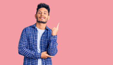 Yakışıklı, Latin Amerikalı, rahat tişört giyen, gülümseyen, mutlu, eli ve parmağı yanda olan genç bir adam. 