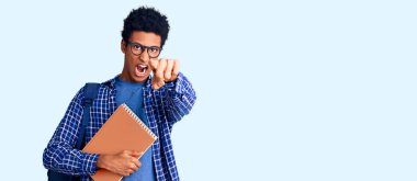 Genç Afrikalı Amerikalı bir adam, elinde öğrenci çantası olan bir kitapla kameraya kızgın ve sinirli bir şekilde bakıyor. 