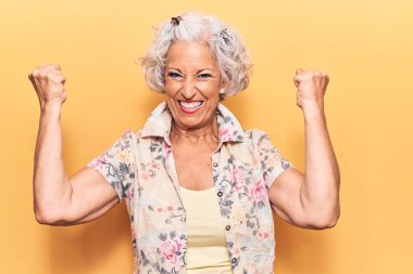 Kıdemli gri saçlı kadın gündelik kıyafetler giyip gururla bağırıyor, zaferi kutluyor ve kollarını kaldırarak çok heyecanlanıyor. 