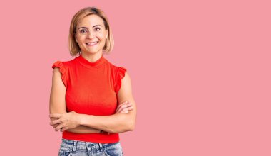 Sıradan kıyafetler giyen, kollarını kavuşturup kameraya bakan mutlu yüzlü genç sarışın kadın. pozitif kişi. 