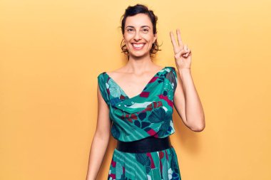 Genç ve güzel İspanyol kadın, sıradan bir elbise giyip kameraya bakıp gülümsüyor ve zafer işareti yapıyor. İki numara.. 