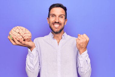 Genç yakışıklı adam hafızasını korumak istiyor beyni izole edilmiş mor arka planda tutarak gururla haykırıyor zaferi ve başarıyı kutluyor.