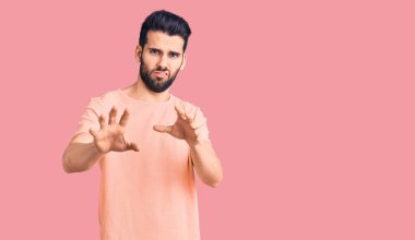 Sakallı, sıradan bir tişört giyen, tiksindirici ve tiksindirici bir ifade takınan genç yakışıklı bir adam. Çünkü tiksinti tepkisi veriyor. Eller havada. 