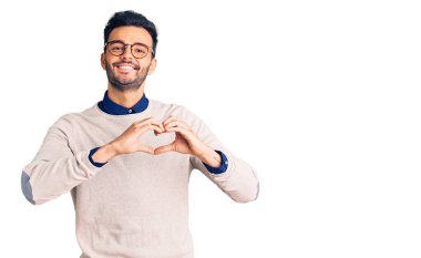 Zarif kıyafetler ve gözlüklerle gülümseyen genç, yakışıklı İspanyol adam elleriyle kalp sembolü yapıyor. romantik kavram. 