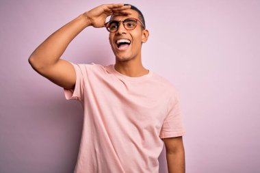 Yakışıklı Afro-Amerikan erkeği pembe arka planda günlük tişört ve gözlük takıyor çok mutlu ve gülümsüyor. Konsept aranıyor.