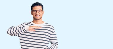 Latin kökenli yakışıklı genç adam, günlük kıyafetler ve gözlük takıyor. Elleriyle büyük ve büyük bir işaret gösteriyor. Ölçüm sembolü. Kameraya bakıp gülümsüyor. ölçüm kavramı. 