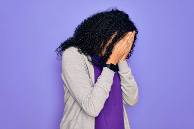 Genç Afro-Amerikan sporcu kadın mor arka plan üzerine sıradan bir sweatshirt giyiyor ve ağlarken suratını ellerle kapatıyor. Depresyon kavramı.