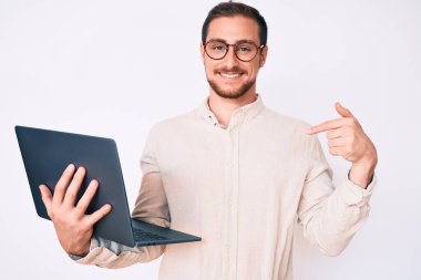 Genç ve yakışıklı bir adam dizüstü bilgisayarını gösterip mutlu ve gururlu bir gülümsemeyi işaret ediyor. 
