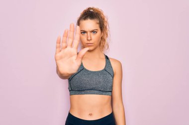 Genç, sarışın, mavi gözlü spor kadın spor kıyafetleri giyiyor ve avuç içiyle şarkı söylemeyi kesiyor. Yüzünde olumsuz ve ciddi bir jest olan uyarı ifadesi.