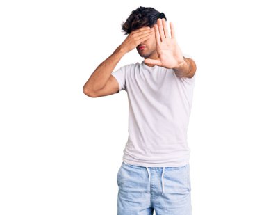 Latin kökenli genç bir adam, günlük kıyafetler giyip, elleriyle gözlerini kapatıyor ve üzgün ve korku ifadeleriyle jestleri durduruyor. utangaç ve olumsuz kavram. 