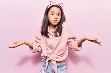 Gündelik kıyafetler giyen, kolları açık ve kafası karışık güzel bir kız çocuğu.. 