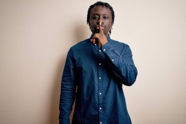 Beyaz arka planda dikilen, rahat gömlekli, genç, Afro-Amerikan bir adam sessiz olmak istiyor. Sessizlik ve gizli konsept.