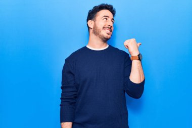 Gündelik kıyafetler giyen, gülümseyen, gülümseyen ve başparmağıyla yan tarafı gösteren İspanyol genç adam.. 