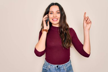 Genç ve güzel bir kadın beyaz arka planda akıllı telefondan konuşuyor. Bir fikir ya da soru işareti ile şaşırdı.