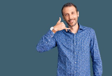 Genç, yakışıklı, sıradan kıyafetler giymiş, gülümseyen, el ve parmaklarıyla telefonla konuşan bir adam. iletişim kavramları. 