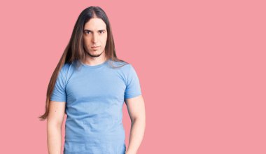 Uzun saçlı, sıradan kıyafetler giyen ve yüzünde ciddi bir ifade olan genç bir adam. Basit ve doğal bir şekilde kameraya bakıyorsun.. 