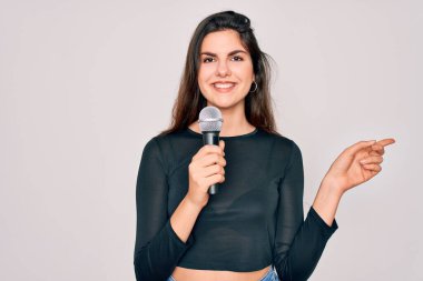 Genç ve güzel şarkıcı kız izole arka planda müzik mikrofonuyla şarkı söylüyor. Elle ve parmakla işaret ederek çok mutlu.