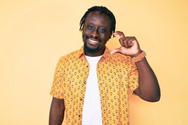 Saçları günlük kıyafetlerle örülmüş, el hareketleriyle küçük boy işaretler yaparak gülümseyen ve kendine güvenen genç Afro-Amerikan bir adam ve kamera. ölçüm kavramı. 