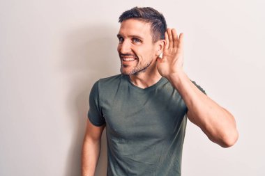 İzole edilmiş beyaz arka planda dikilen sıradan tişörtler giyen genç yakışıklı adam kulağına fısıldayarak dedikodu ya da dedikoduları dinliyor. Sağırlık kavramı.