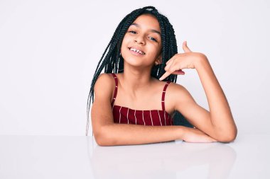 Saçları örgülü, masada oturmuş gülümseyen el ve parmaklarıyla telefonla konuşan, telefonda konuşan Afro-Amerikan kız çocuğu. iletişim kavramları. 