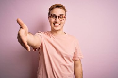 Genç, yakışıklı, günlük tişört giyen, pembe arka planda duran, dostça gülümseyerek selamlaşan bir kızıl adam. Başarılı bir iş..