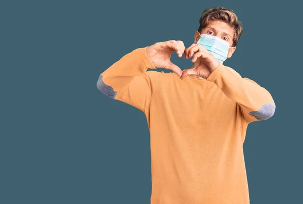 心臓のシンボルと手で形を示す愛に笑みを浮かべて医療用マスクを身に着けている若いハンサムな男 ロマンチックなコンセプト — ストック写真