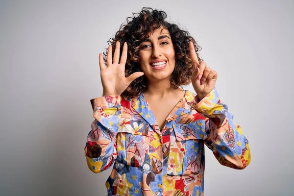 Young beautiful curly arab woman wearing floral colorful shirt standing over white background showing and pointing up with fingers number six while smiling confident and happy.