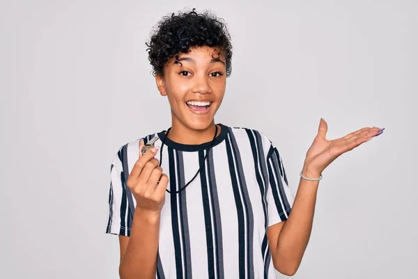 Young beautiful african american afro referee woman wearing striped uniform using whistle very happy and excited, winner expression celebrating victory screaming with big smile and raised hands
