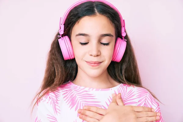 可爱的惊慌失措的小女孩用耳机听着音乐 双手放在胸前笑着 满脸感激地闭上眼睛 健康概念 — 图库照片
