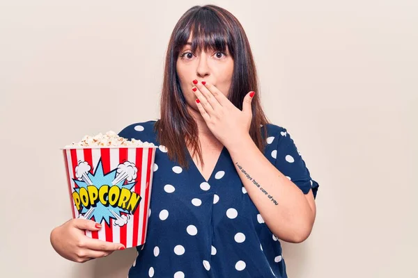 Młoda Kobieta Rozmiarze Trzymająca Popcorn Zakrywający Usta Dłonią Zszokowana Przerażona — Zdjęcie stockowe