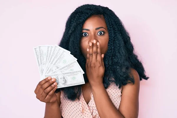 Hermosa Mujer Africana Sosteniendo Dólares Cubriendo Boca Con Mano Conmocionada —  Fotos de Stock