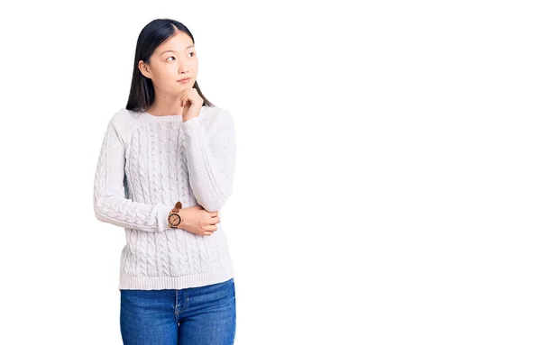 年轻美丽的中国女人穿着宽松的毛衣 手托着下巴思考着问题 沉思着表情 微笑和体贴的脸 怀疑概念 — 图库照片